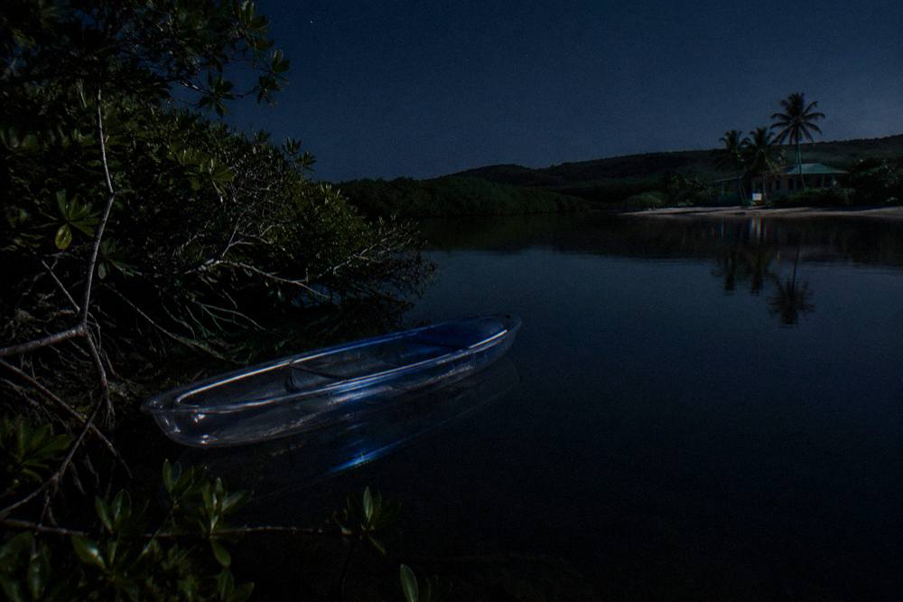 A clear kayak on dark calm water in a tropical bay at night