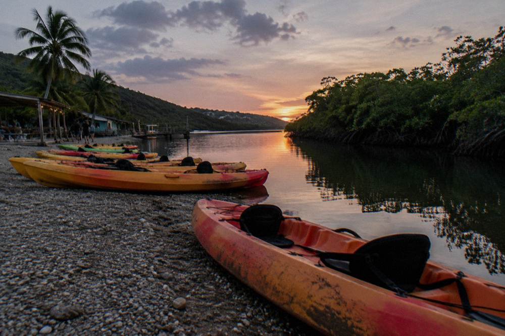 Tandem kayaks lined up on a shoreline beside a channel of still dark water