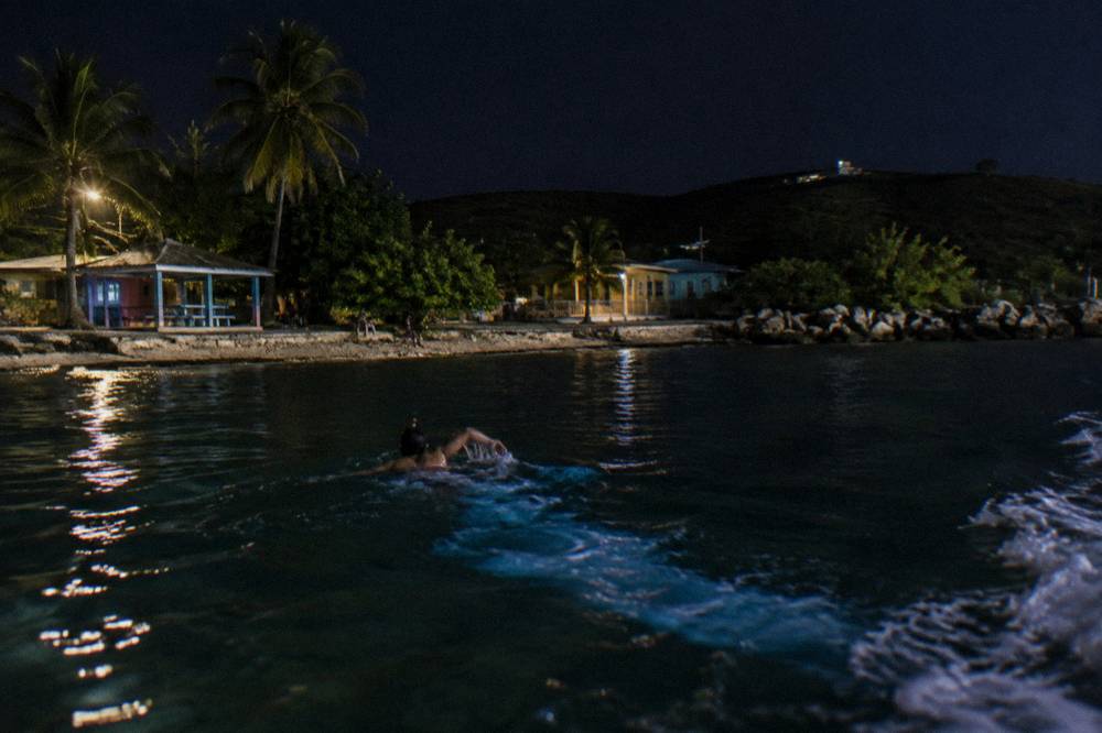A hand trailing through dark water leaving a faint blue streak of light