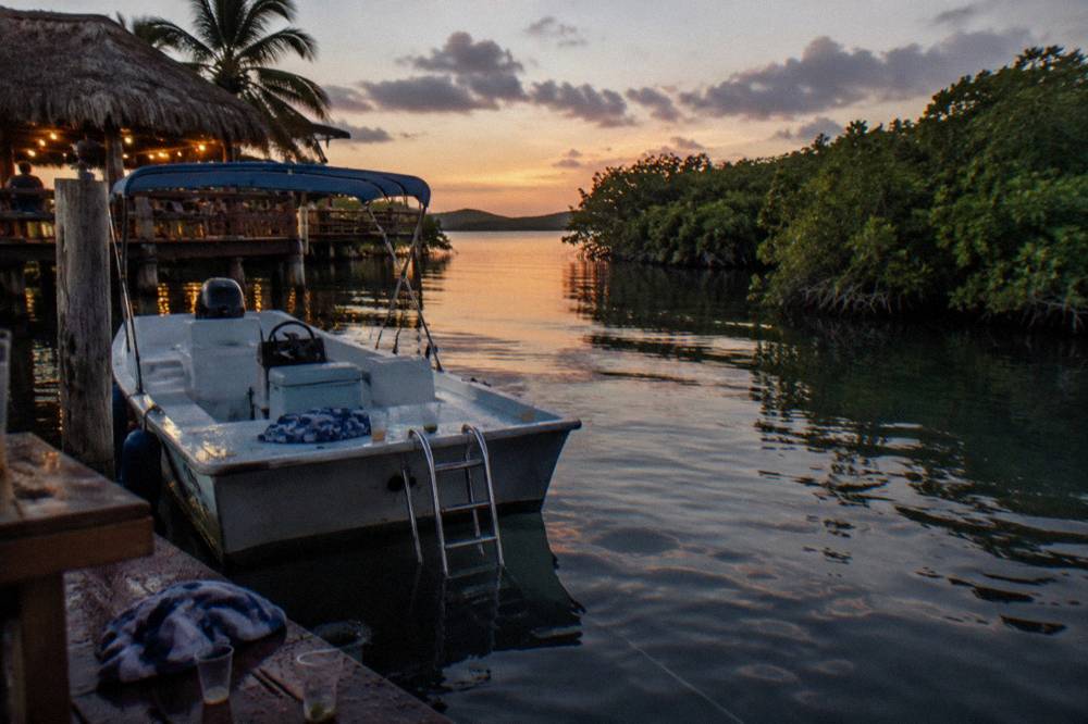 Dark evening water in a small boat-filled Caribbean bay with lights along a distant shore