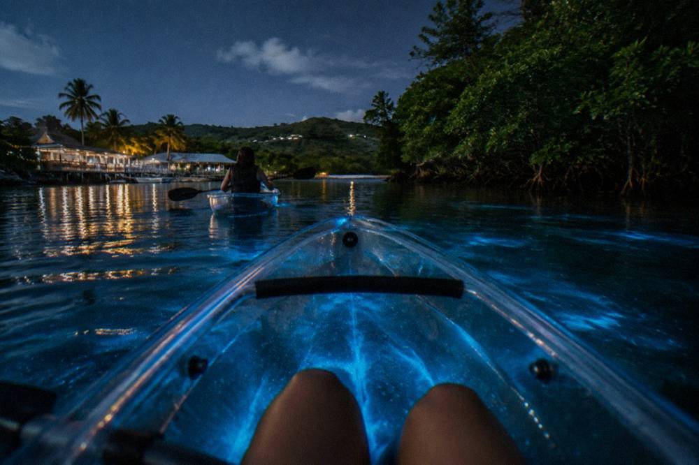 Clear bottom kayak gliding over faint blue light in calm night water