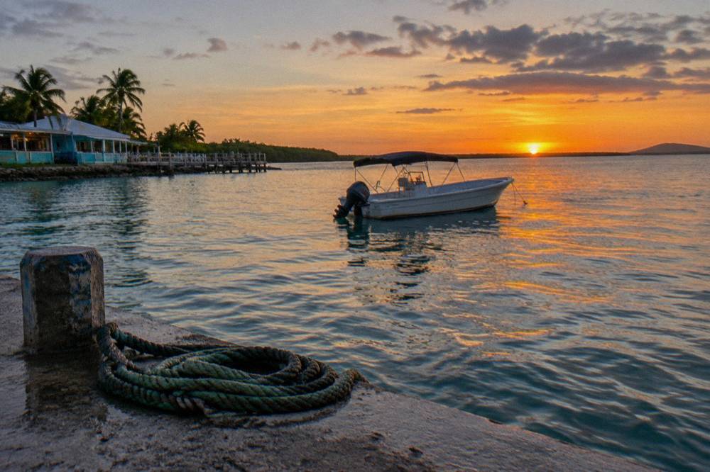 A small boat floating on dark calm water with a sunset sky above the horizon