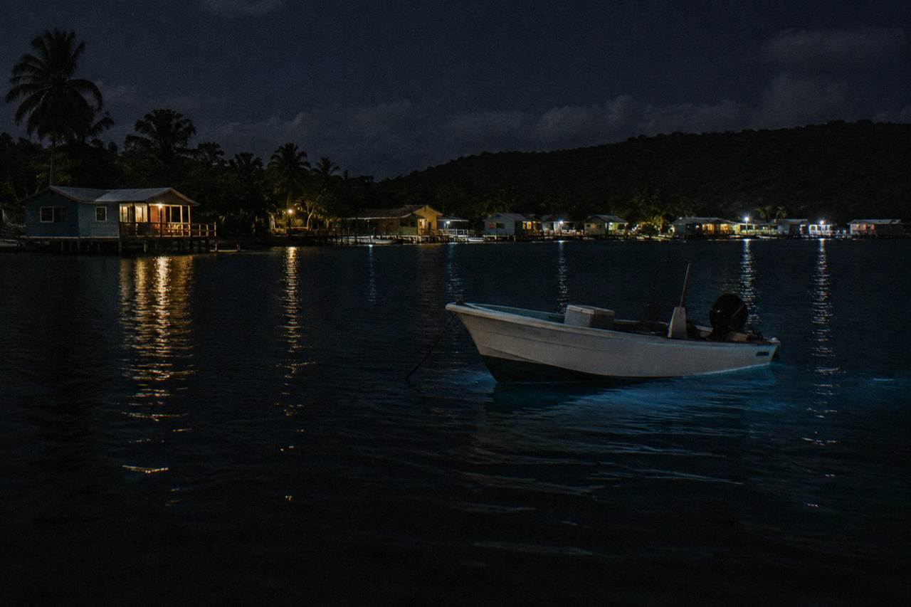 A calm boat anchored in a dark lagoon at night with faint blue light on the water