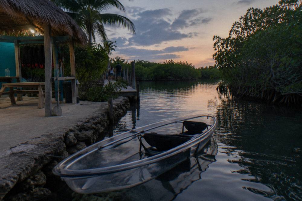 Clear bottom kayak resting on dark water in a narrow mangrove channel at dusk