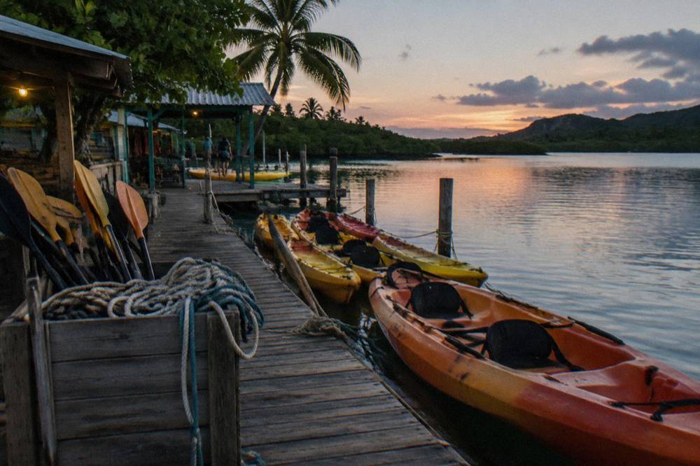 Clear kayaks floating on dark calm water with faint blue light trailing the paddle strokes