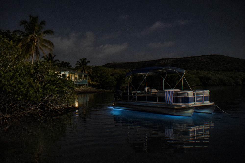 A calm mangrove channel at night with kayak lights in the distance and dark still water