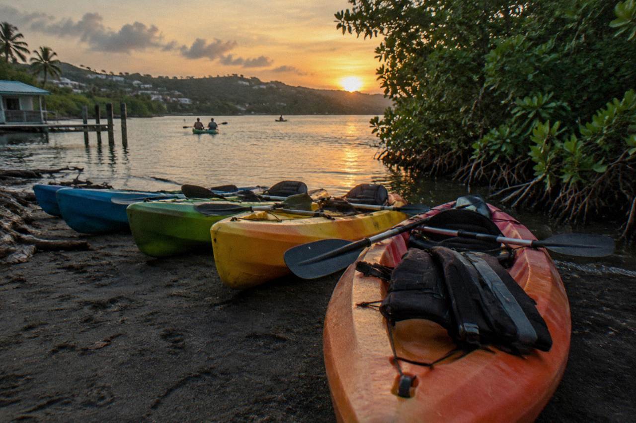 Tandem kayaks lined up on a dark shoreline beside calm lagoon water at dusk