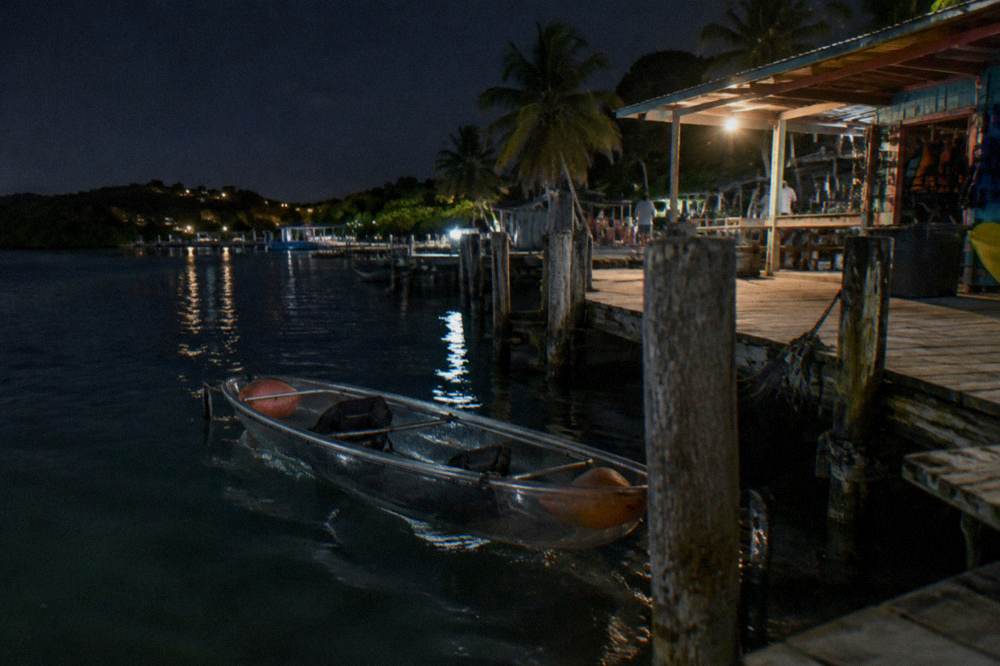 Clear bottom kayak resting on dark water beside a wooden dock at night