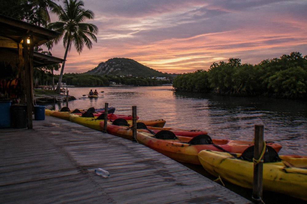 Tandem kayaks lined up on a dock beside calm dark water at dusk