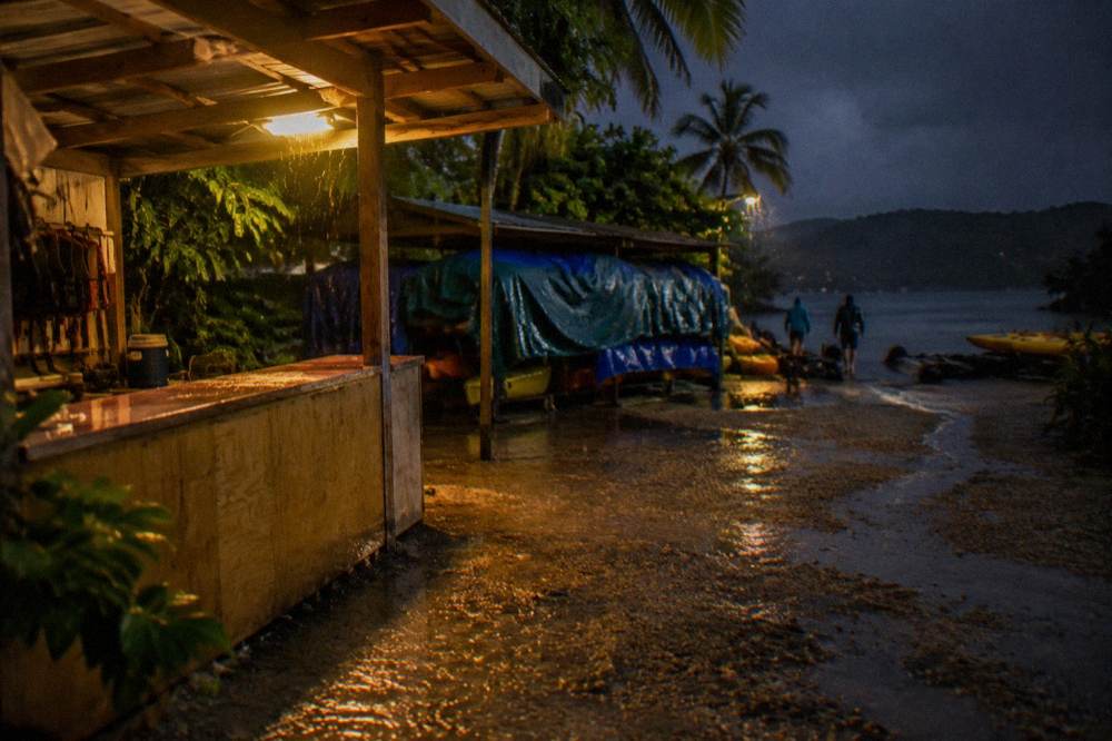 A tour operator's kiosk lit by a warm lamp beside a dark waterfront at night