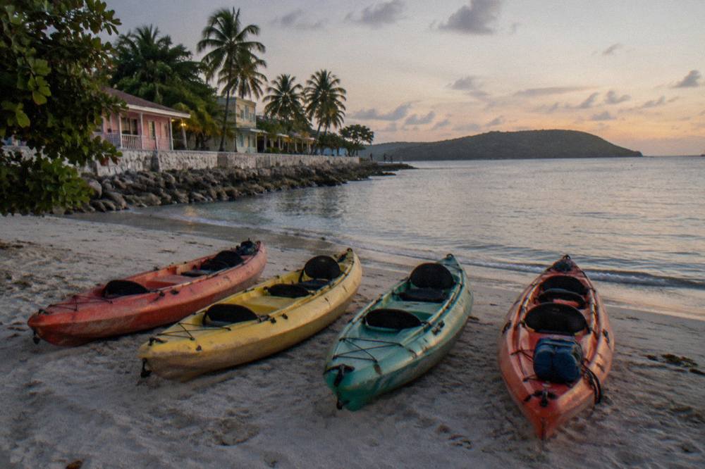 Tandem kayaks lined up on a beach beside calm water before a night tour