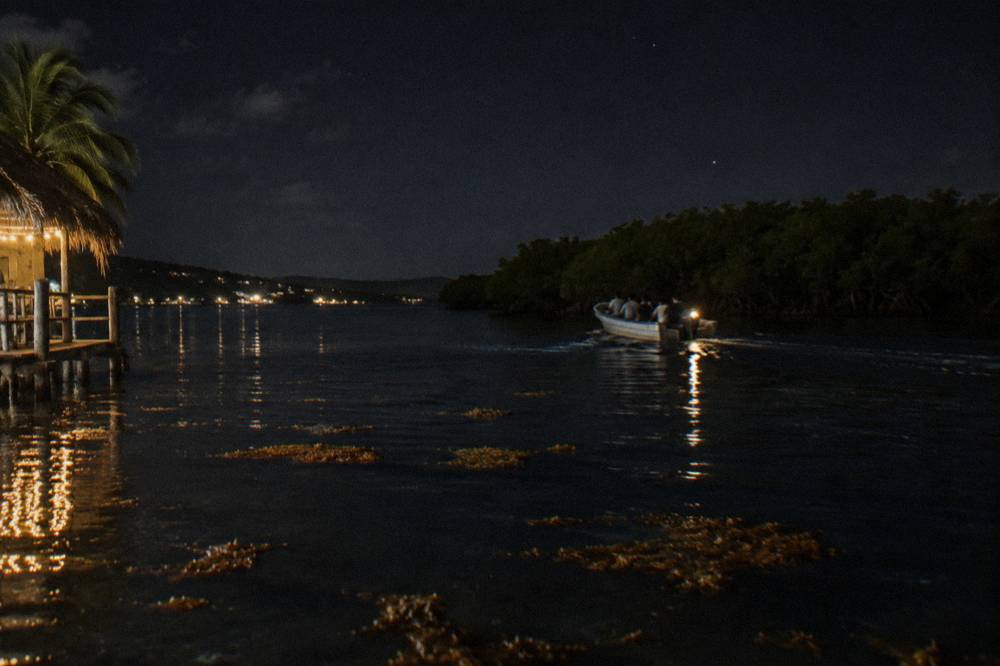 A small boat with passengers moving across a dark lagoon at night