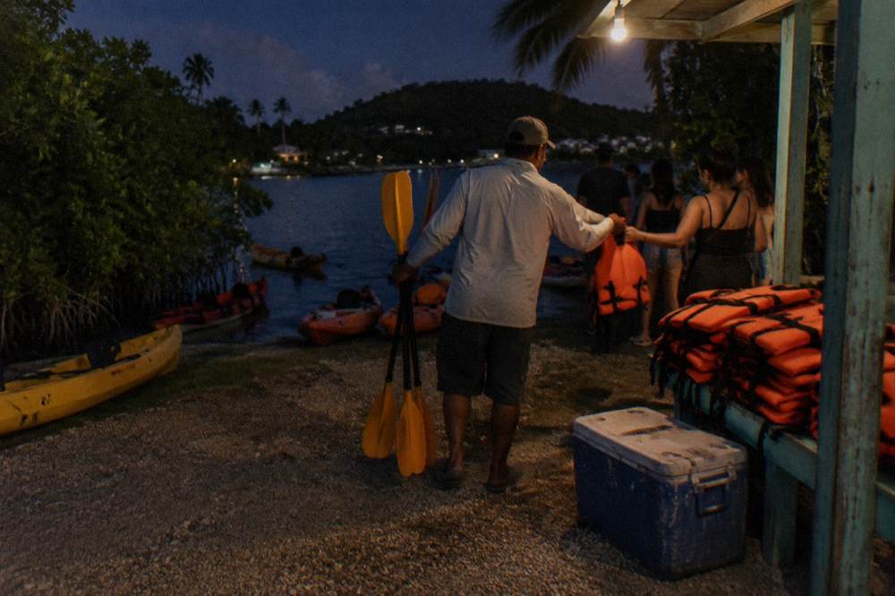 A guide handing paddles and life vests to guests at a night tour meeting point
