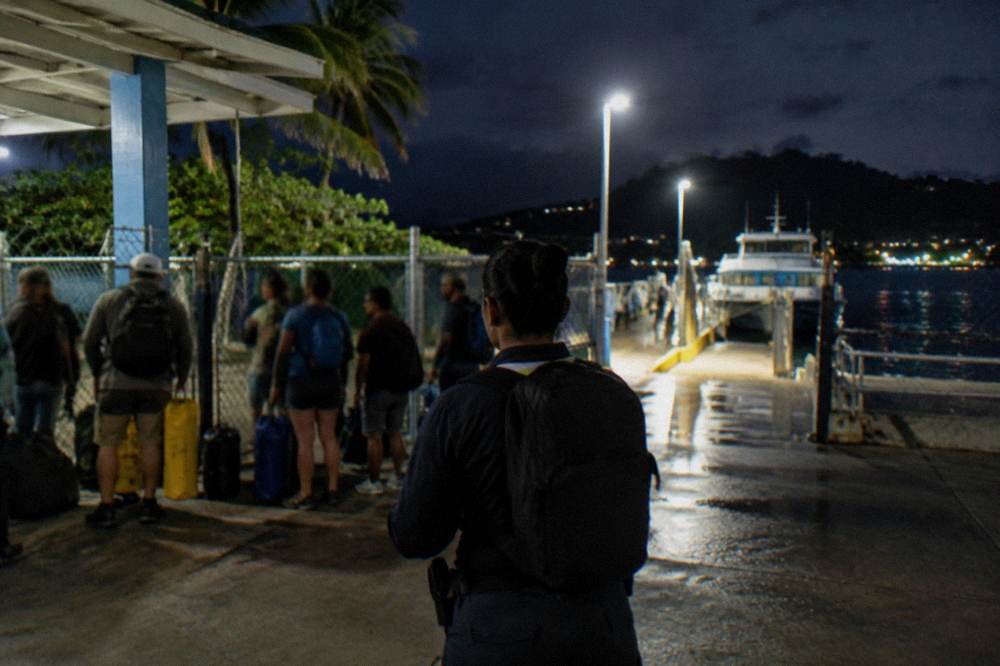 Tour guide checking a clipboard with guests gathered at a waterside kiosk at night