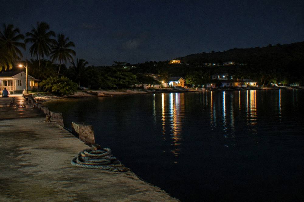 Boat lights reflecting on dark calm water at a small dock at night