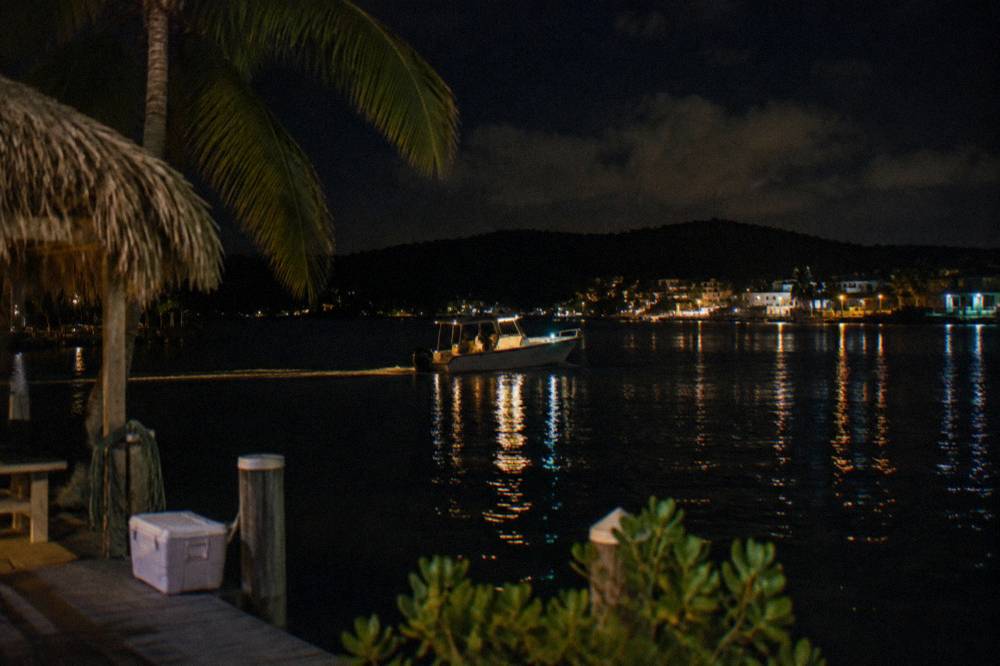 A small motorboat crossing a calm bay at night with cabin lights on