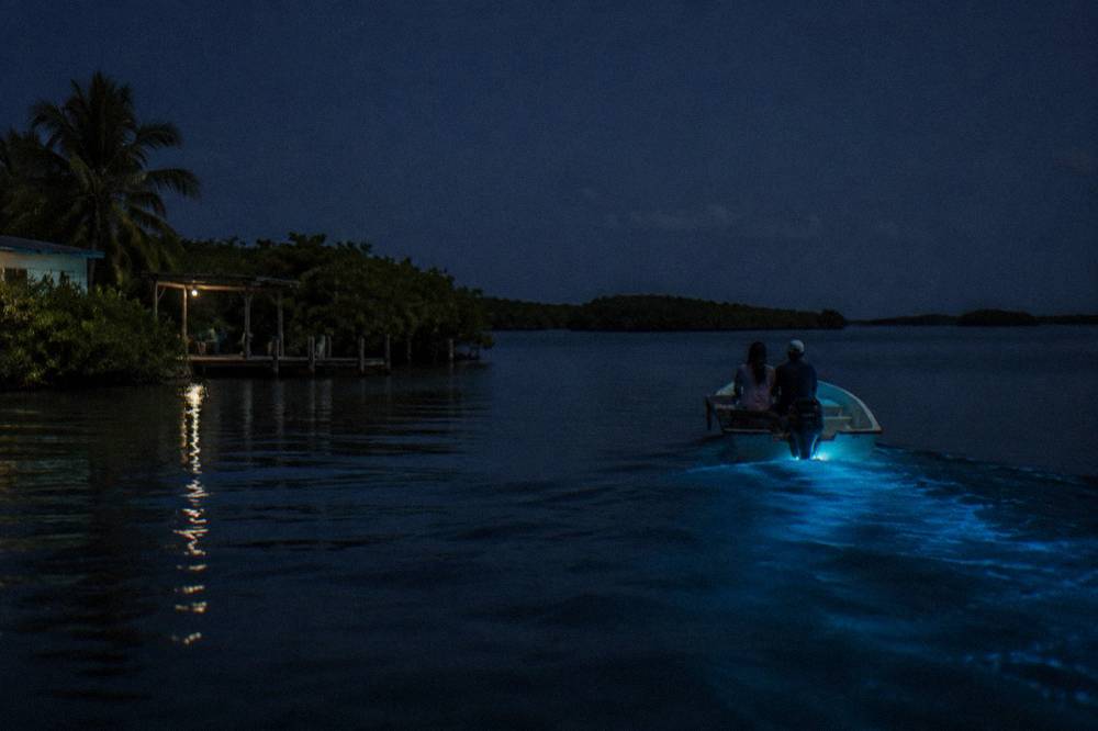 A small motorboat at night on calm water with a soft blue glow trailing behind the hull