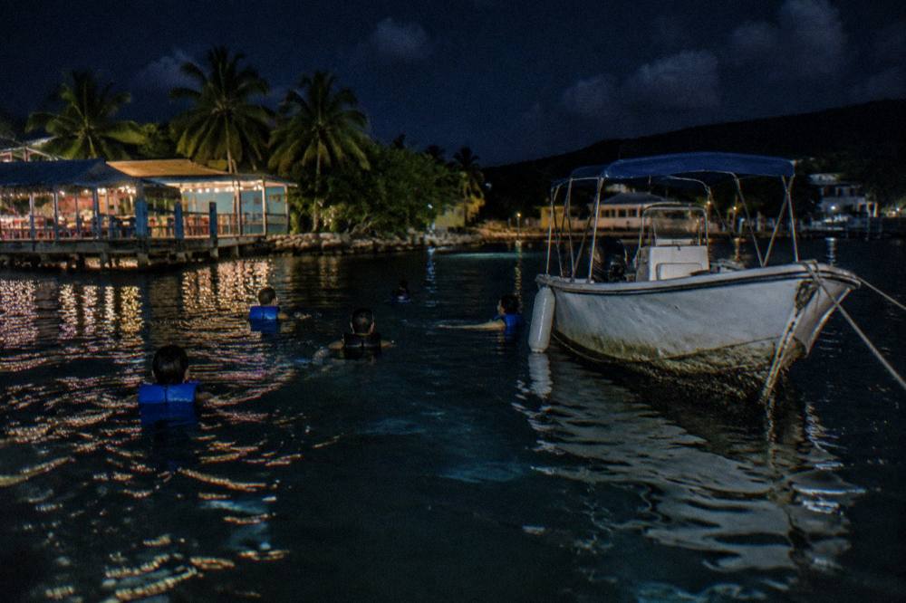 Swimmers in life vests floating on dark water beside a small anchored boat