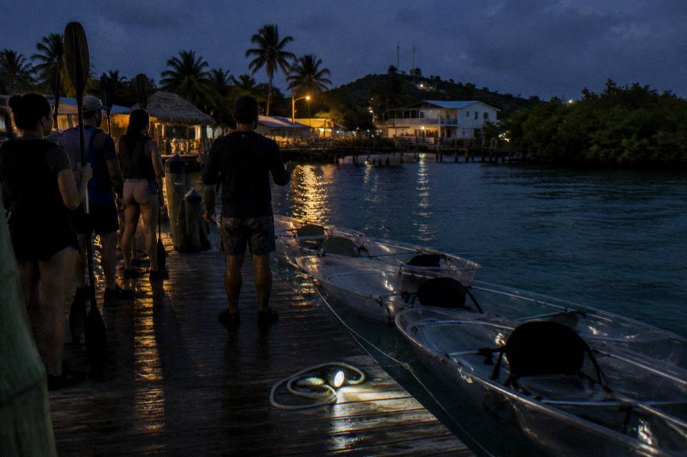 A guide briefing a small group holding paddles beside transparent kayaks at a dock at night