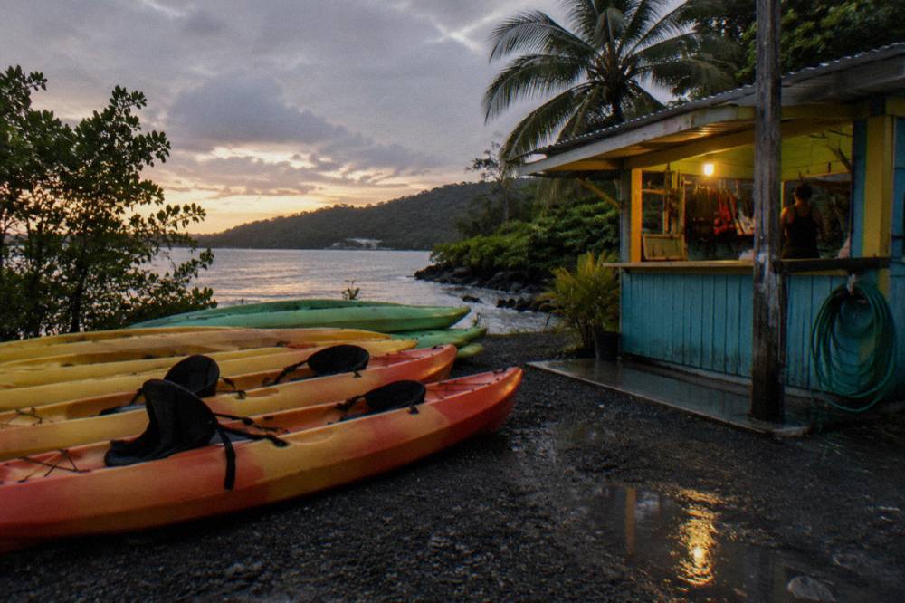 Tandem kayaks lined up on a dark shoreline beside a small wooden kiosk before a night tour