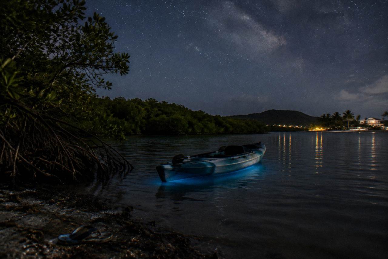 A kayak floating on a dark lagoon under a starry sky, with faint bioluminescent glow in the water.