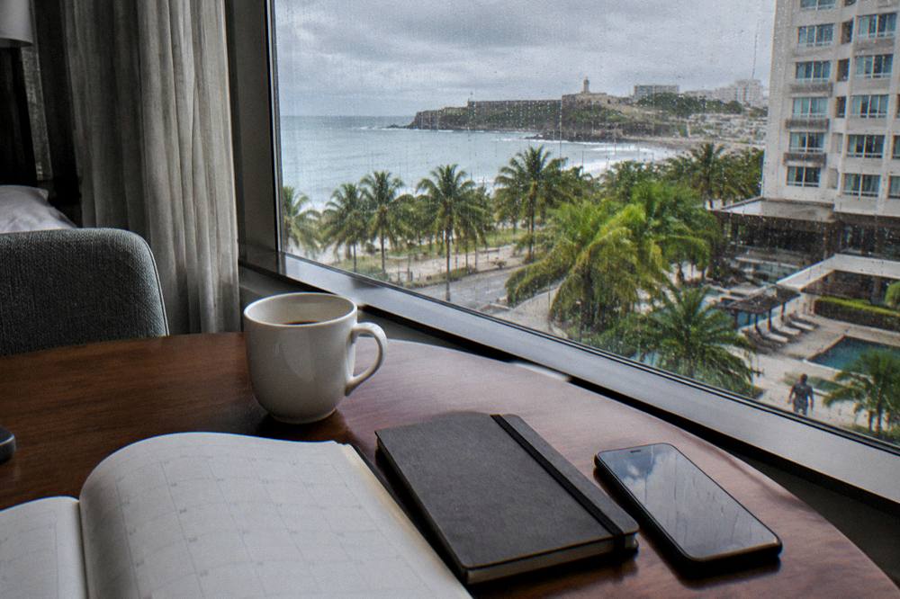 A calendar and notebook beside a phone on a wooden table near a window